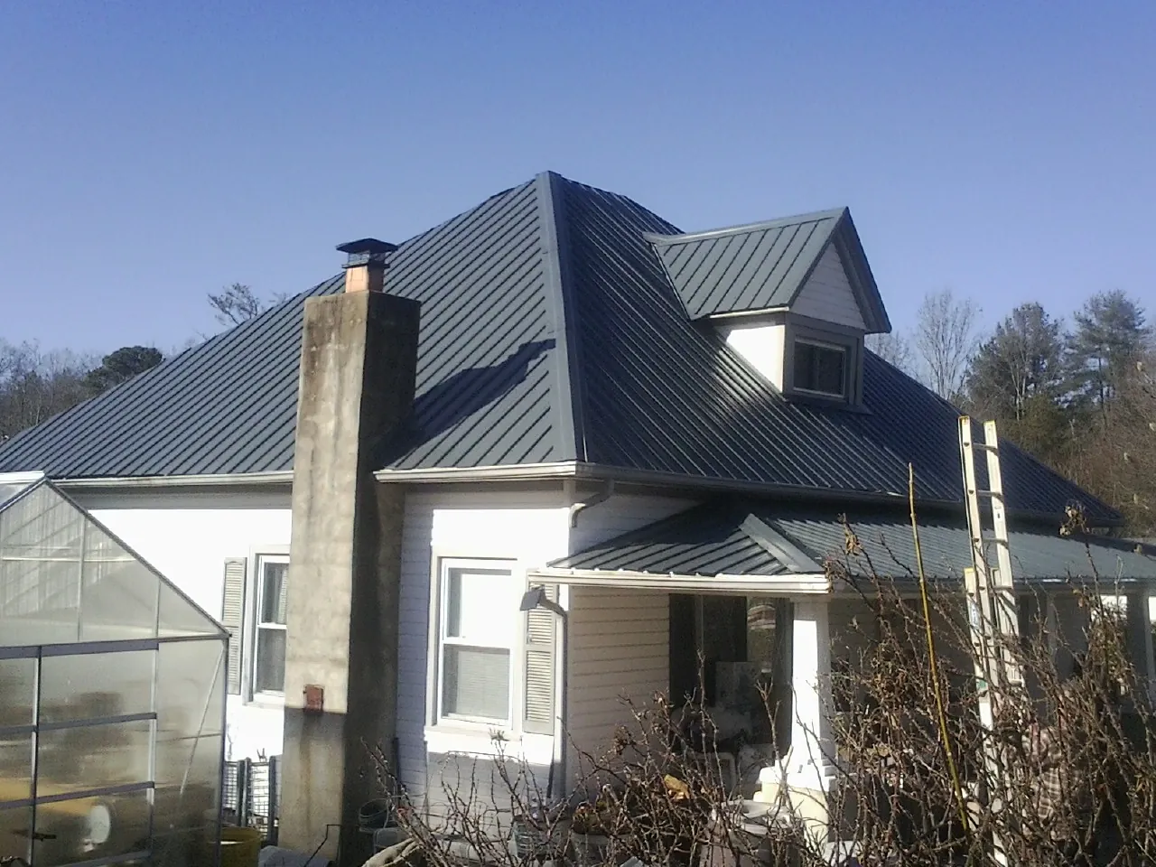 Dark blue standing seam metal roof on a white farmhouse with dormer — Slate & Tile Roof Repair by Roofing Brothers in Chinook