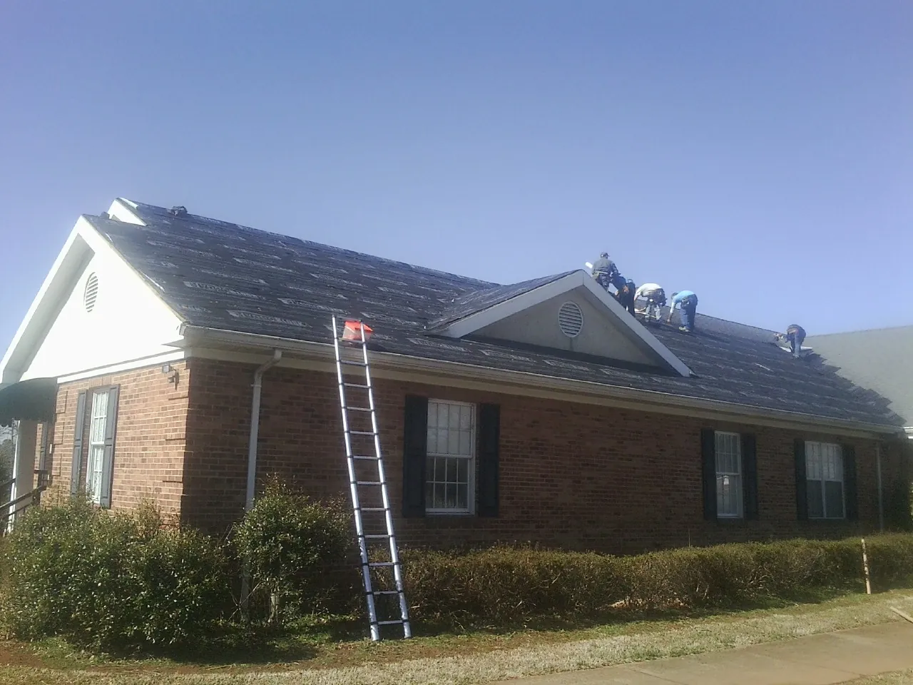 Crew tearing shingles off a brick ranch roof with a ladder set — Emergency Roof Repair work by our crew in Chinook