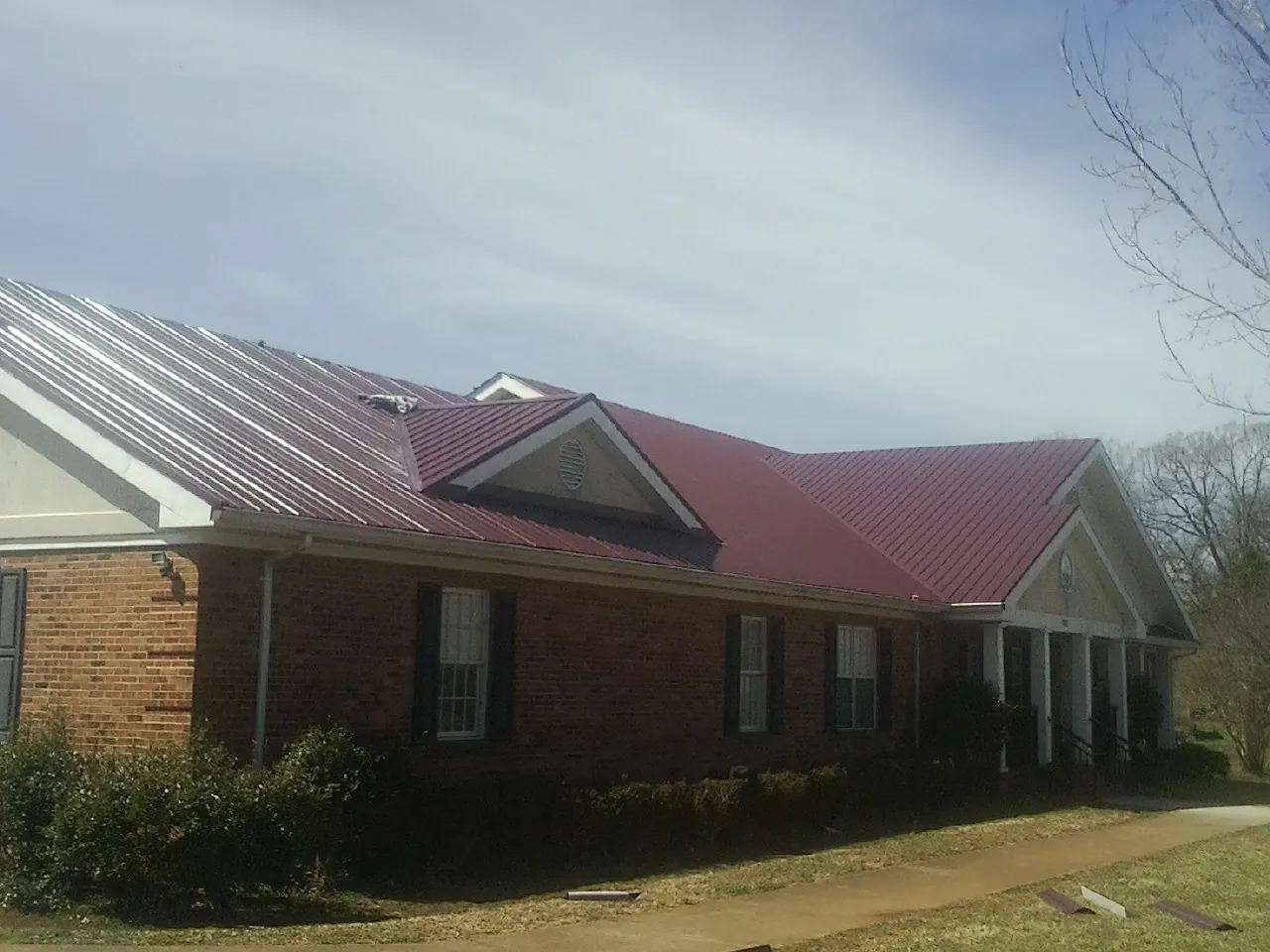 Red metal roof with gabled entries on a long brick building, from a Hail Damage Roof Repair job in Chinook