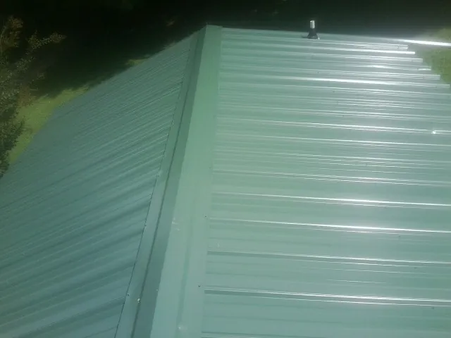New green metal panels meeting at the ridge of a roof — Flat Roof Repair work by our crew in Chinook