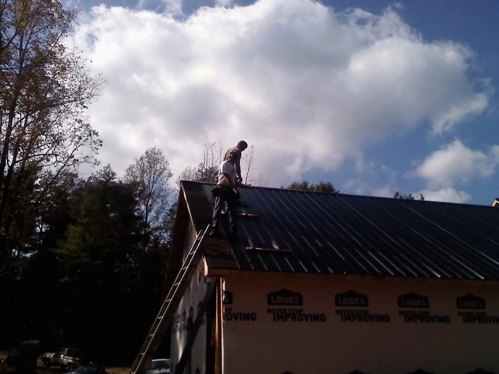 Roofer fastening dark metal panels high against a cloudy sky, from a Roof Inspection job in Chinook