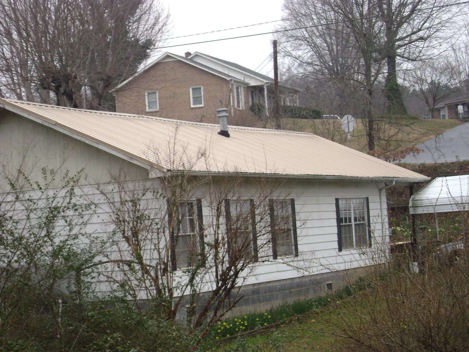 Tan metal roof on a white sided house set into a hillside — Commercial Roofing by Roofing Brothers in Chinook